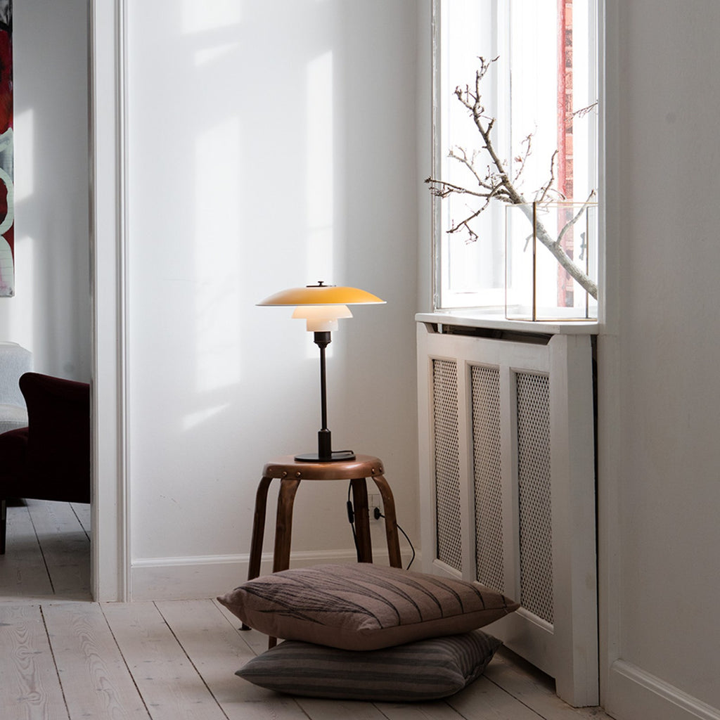 The PH 3½-2½ table lamp is designed based on the principle of a reflective three-shade system, which directs the majority of the light downwards. The shades are made of mouth-blown opal three-layer glass, which is glossy on top and sandblasted matt on the underside, giving a soft and diffuse light distribution. Designed by Poul Henningsen.
